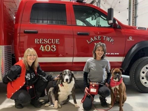 Franciscan Health Pet Therapy Program volunteers Julie Canady, left, with Meiko and Paulette Bedka with Darla in front of Lake Township Volunteer Fire Department truck.
