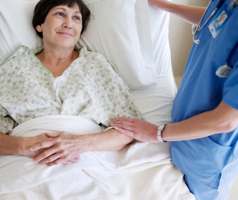 Woman lying in hospital bed with nurse gently holding her arm in comfort
