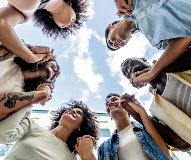 a view looking up at a huddle of people holding hands and the sky