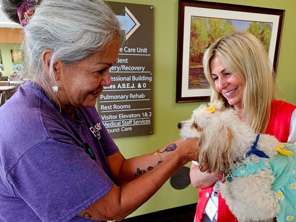 Health Munster Environmental Services Associate Diane Sandoval, left, pets Mary Hires’ dog, Molly, during a visit from the Pet Therapy Program earlier this year.