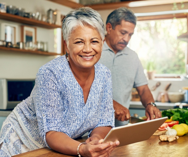 elderly couple in kitchen, woman holding a tablet device